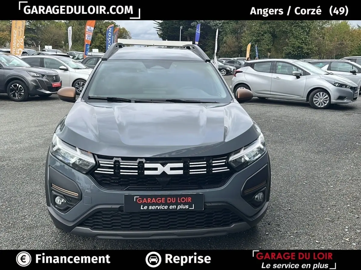 Vue avant d'un Dacia Jogger Extreme+ Hybrid 140 2025 gris foncé avec calandre noire et détails bronze, sur parking extérieur.