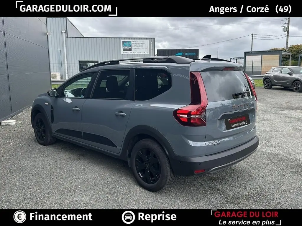 Vue 3/4 arrière droite d'un Dacia Jogger Extreme+ Hybrid 140 gris avec jantes noires, en extérieur sur parking.