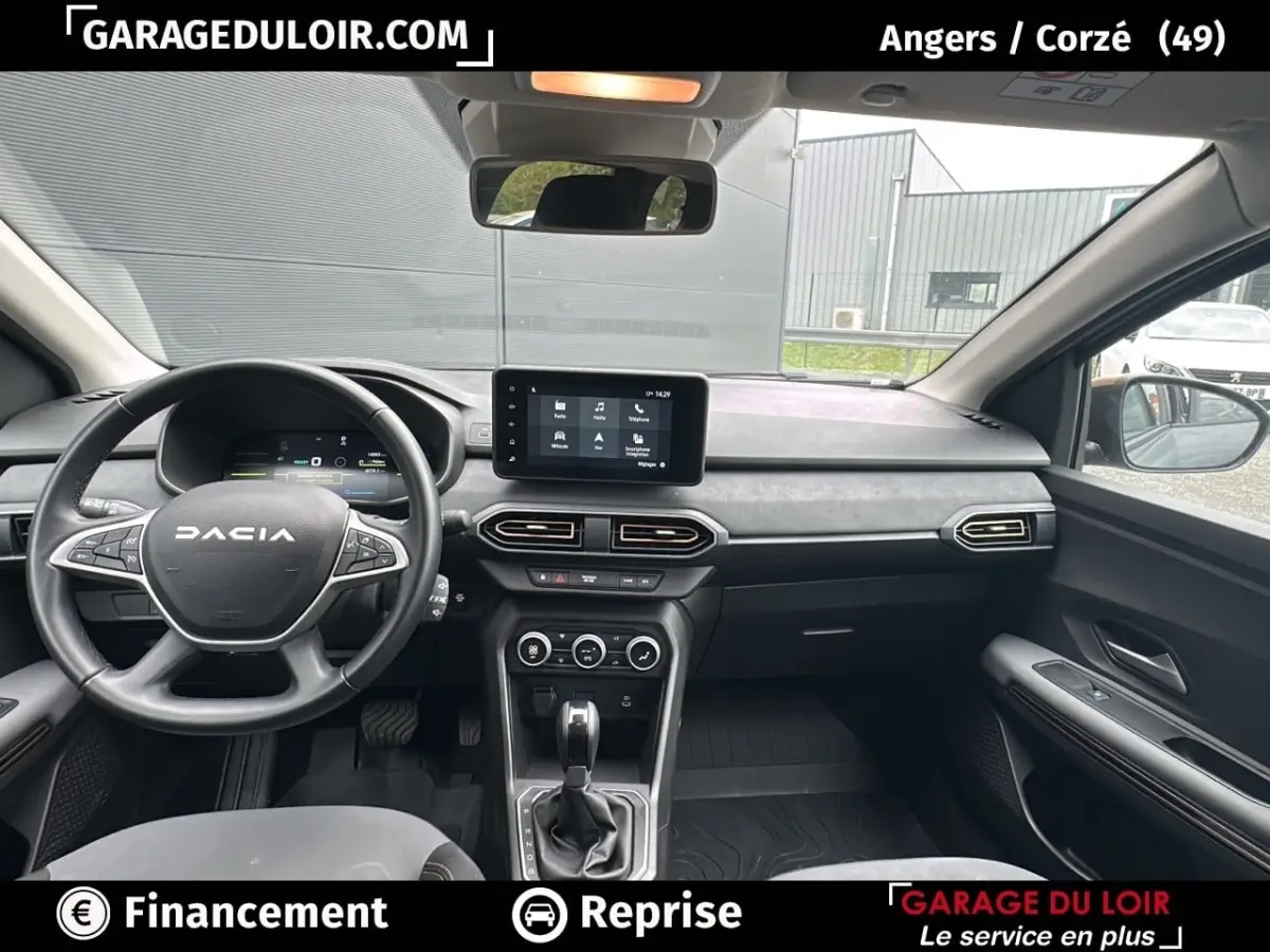 Vue intérieure avant du Dacia Jogger Extreme+ Hybrid 140 2025, tableau de bord gris avec écran tactile central et volant multifonction.