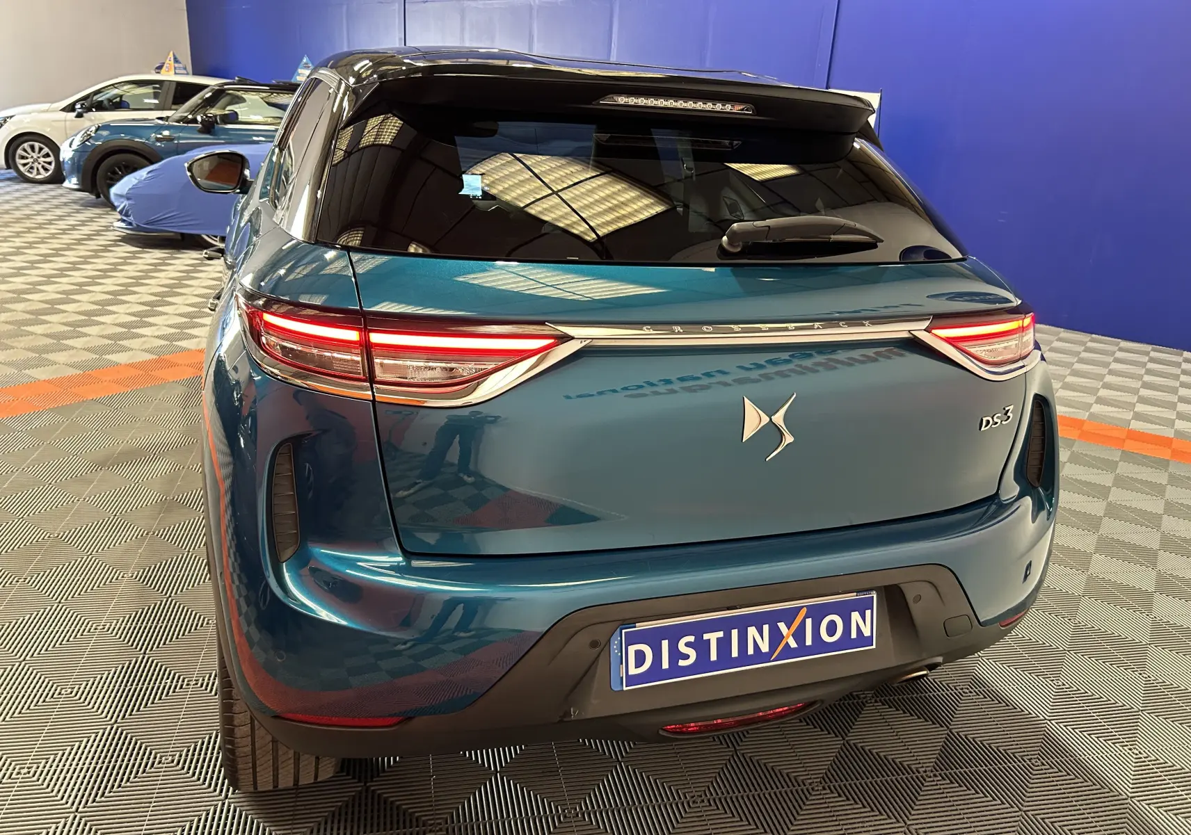 Vue 3/4 arrière d'un DS3 Crossback bleu Millenium avec feux LED allumés dans un showroom.