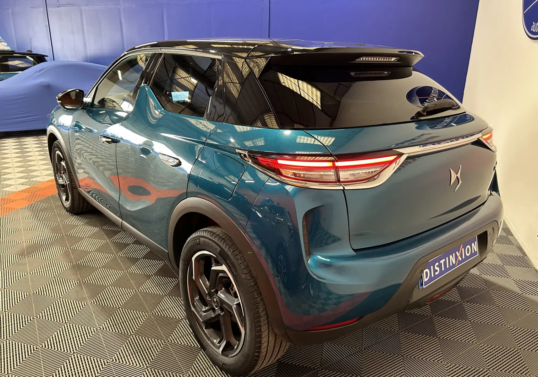 Vue 3/4 arrière droite du DS3 Crossback bleu Millenium avec toit noir et feux arrière allumés dans un showroom.