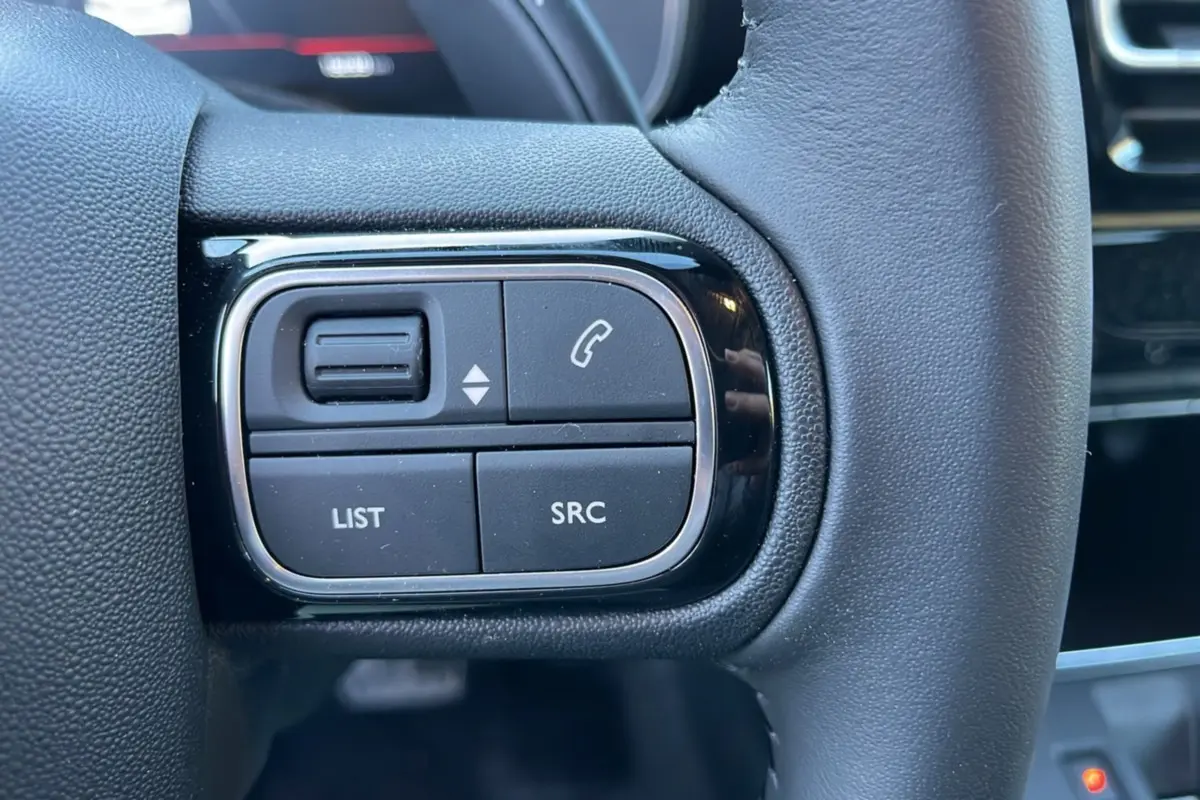 Gros plan sur les commandes gauche du volant cuir noir du Citroën C5 Aircross Hybrid 2025.