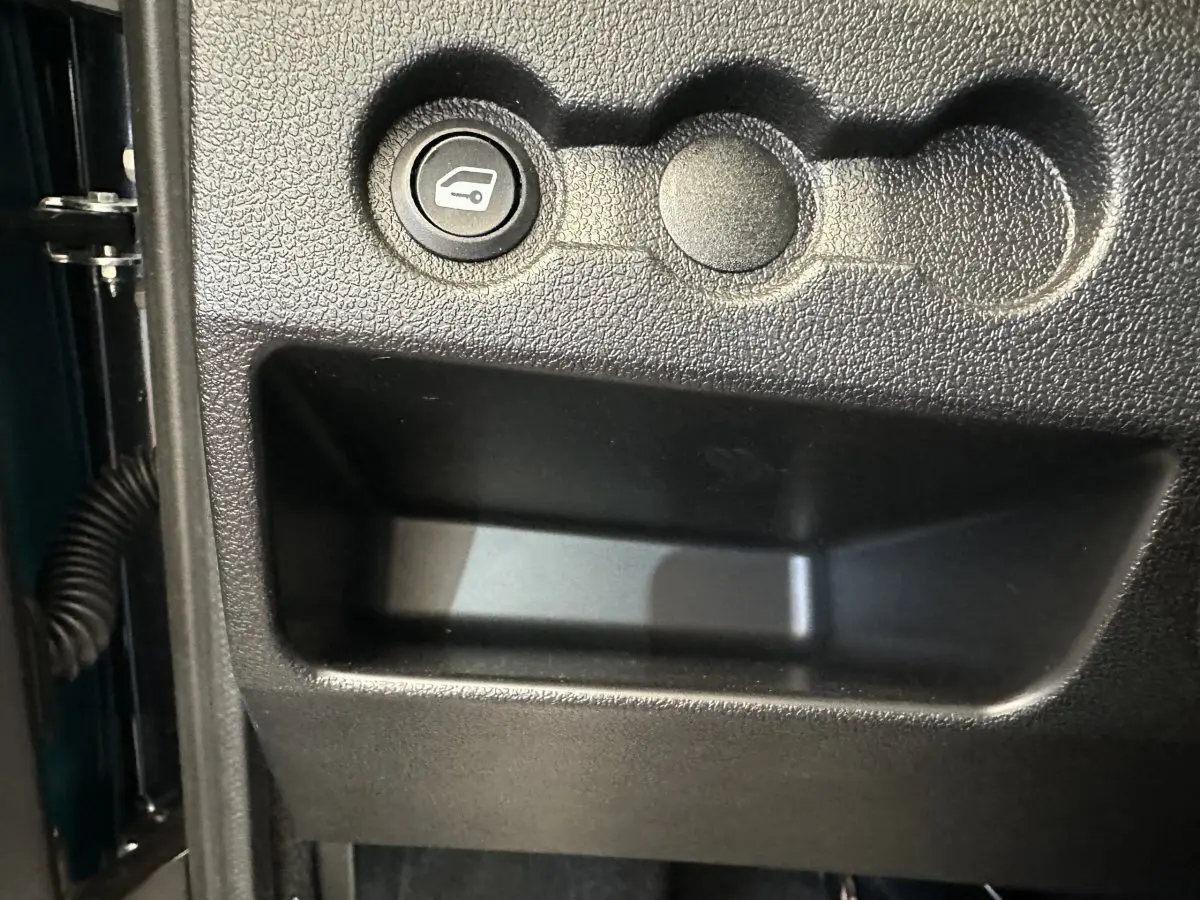 Gros plan sur le bouton d'ouverture du coffre dans l'habitacle d'une Aixam Ambition 0.5 City Pack bleu 2025.