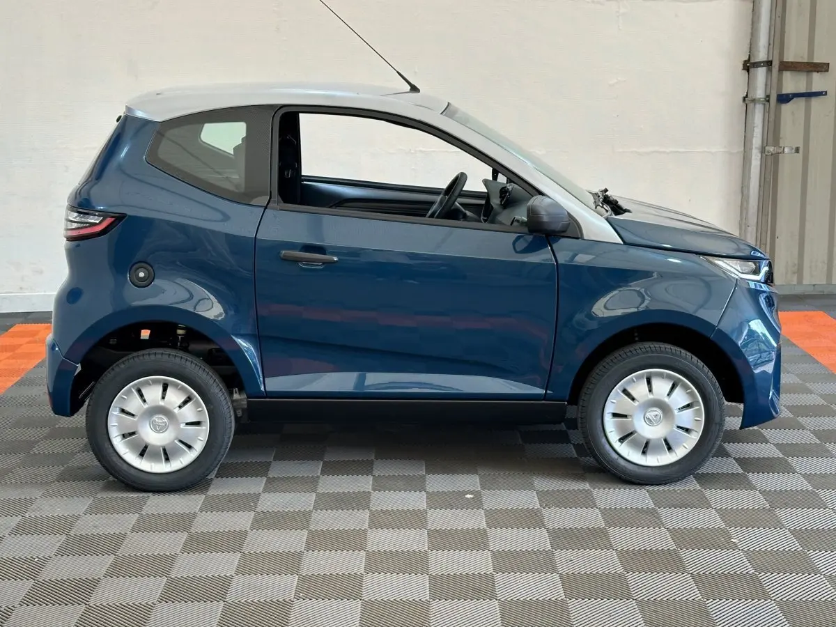 Profil côté droit de l'AIXAM AMBITION 0.5 CITY PACK 2025 bleu avec toit blanc et rétroviseur caméra côté conducteur.