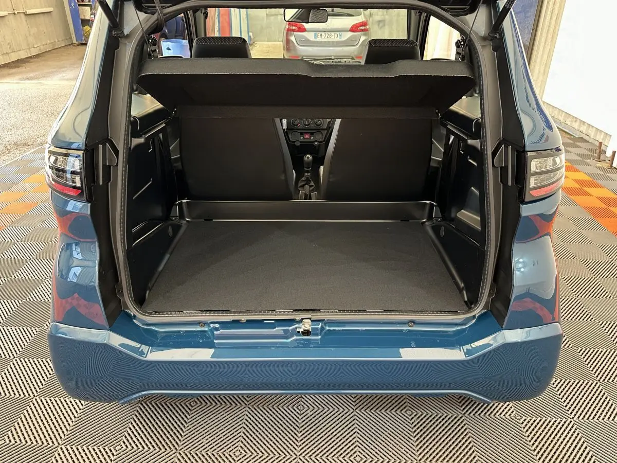 Vue arrière ouverte du coffre d'une Aixam Ambition 0.5 City Pack bleu 2025, avec intérieur spacieux et banquette visible.