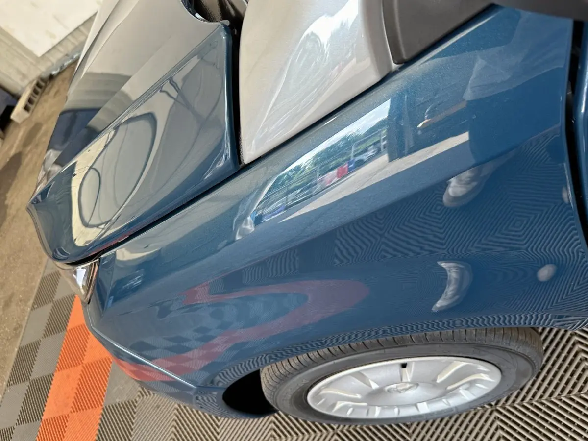 Gros plan sur l'aile avant gauche bleu d'une Aixam Ambition 0.5 City Pack avec rétroviseur caméra côté conducteur.