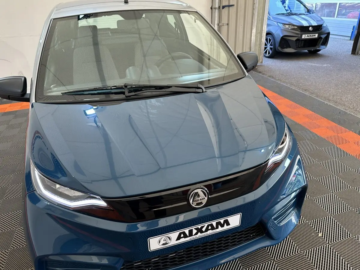 Vue avant rapprochée d'une Aixam Ambition 0.5 City Pack bleu 2025 avec calandre noire et phares LED marqués.