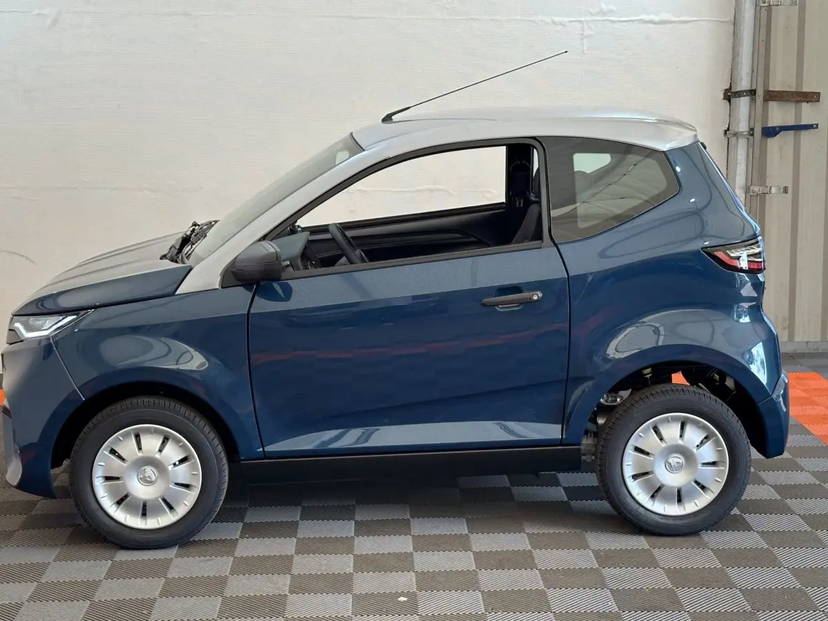 Profil côté gauche de l'AIXAM AMBITION 0.5 CITY PACK 2025 bleu avec toit blanc et rétroviseur caméra conducteur.