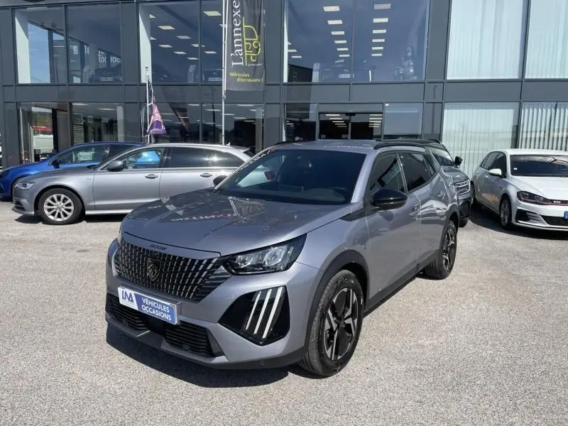 Peugeot 2008 gris métal vue 3/4 avant avec calandre noire distinctive et feux LED verticaux, stationné devant un showroom.