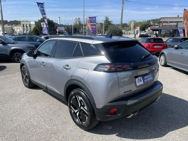 Vue 3/4 arrière droite d’un Peugeot 2008 gris métal 2025 avec jantes noires et vitres teintées, stationné en extérieur.