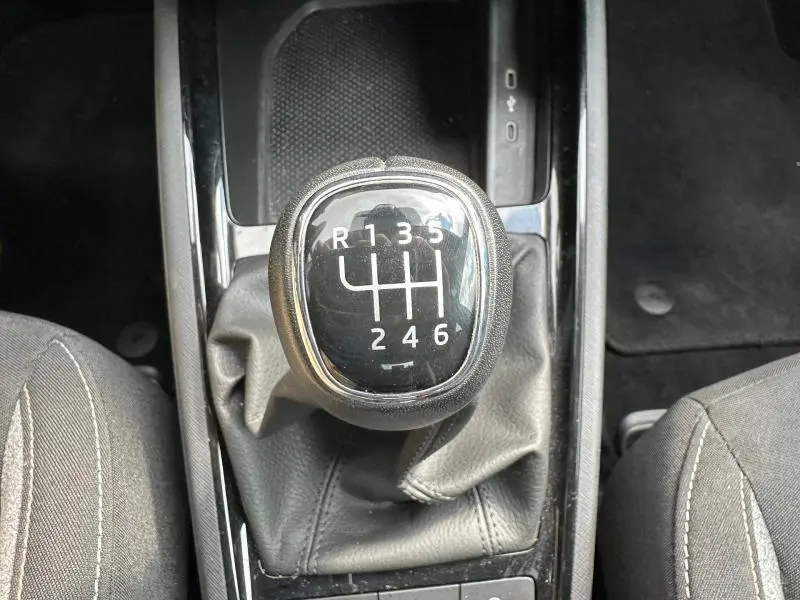 Gros plan sur le levier de vitesse manuel noir avec surpiqûres, intérieur tissu gris du Skoda Scala blanc cristal.