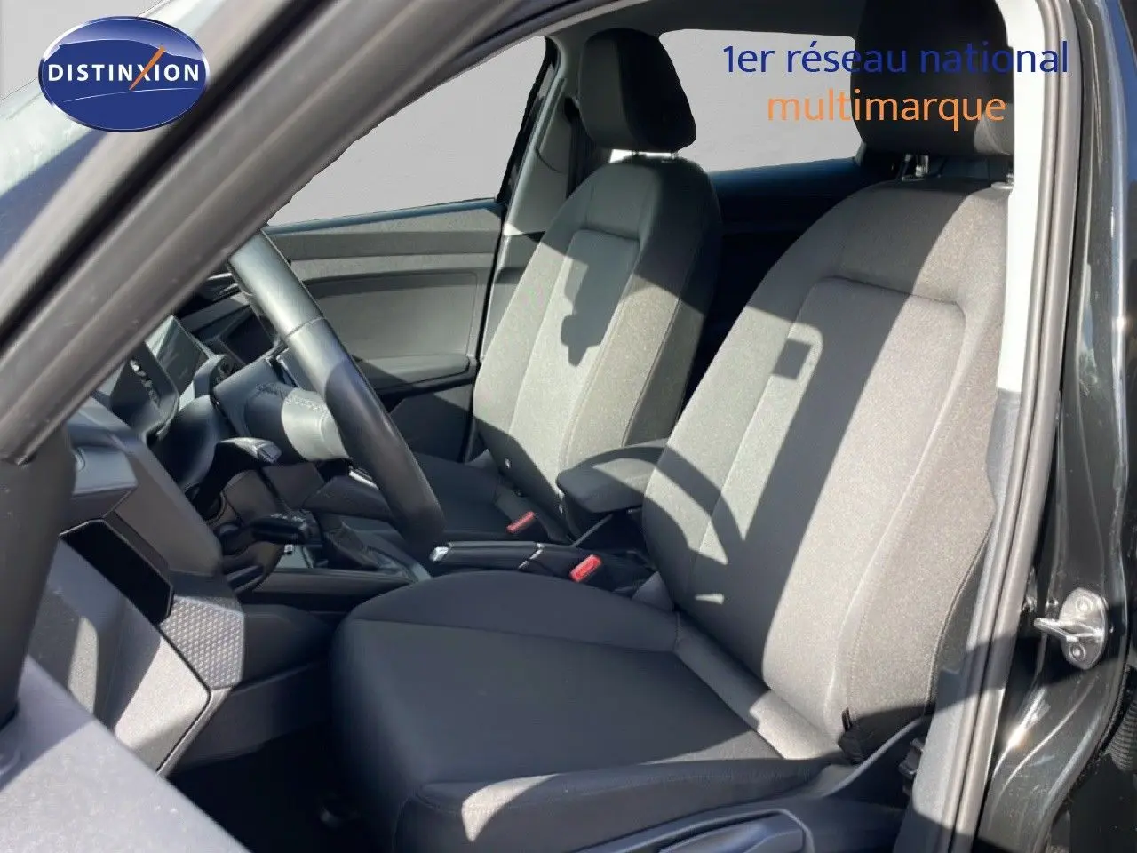 Vue intérieure côté conducteur de l’Audi A1 Sportback 2023 noir Mythe Metal, avec sièges tissu gris et volant cuir.