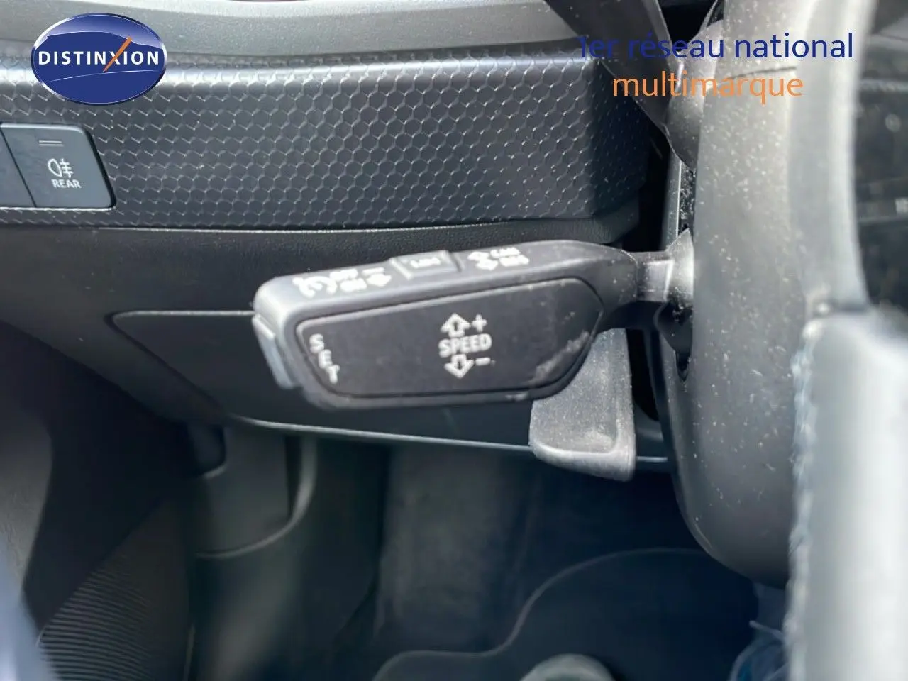 Gros plan sur la commande de régulateur de vitesse à gauche du volant d’une Audi A1 Sportback noire, intérieur sombre.
