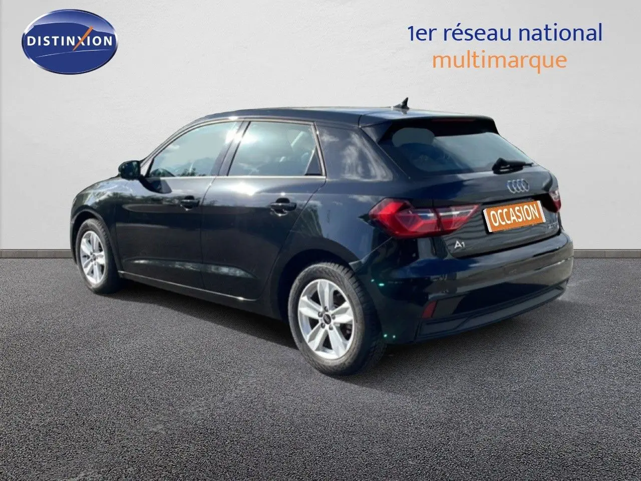 Audi A1 Sportback noir mythe métal vue 3/4 arrière droit sur sol gris avec logo Distinxion en arrière-plan.