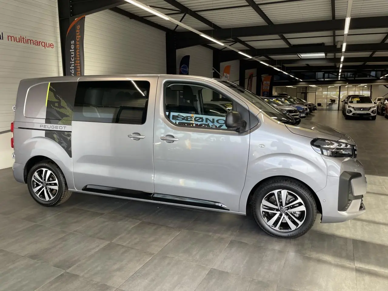 Vue de profil côté droit du Peugeot Expert Fourgon gris Artense avec décor adhésif noir et jaune à l'arrière.