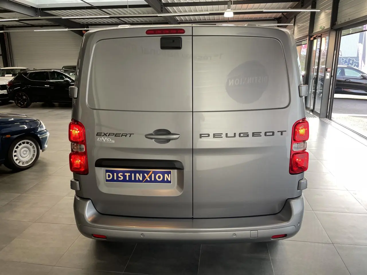 Vue arrière du Peugeot Expert Fourgon gris Artense avec portes battantes et feux allumés en intérieur showroom.