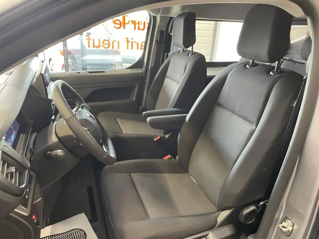 Vue intérieure côté conducteur du Peugeot Expert Fourgon gris Artense, montrant les sièges avant noirs et le volant multifonction.
