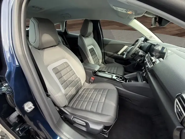 Vue intérieure côté conducteur de la Citroën C4 hybride 2025 bleu, sièges tissu gris avec console centrale moderne.