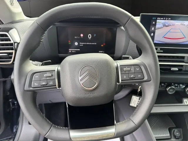 Vue rapprochée du volant cuir multifonctions de la Citroën C4 hybride 2025 avec tableau de bord digital et écran de recul.