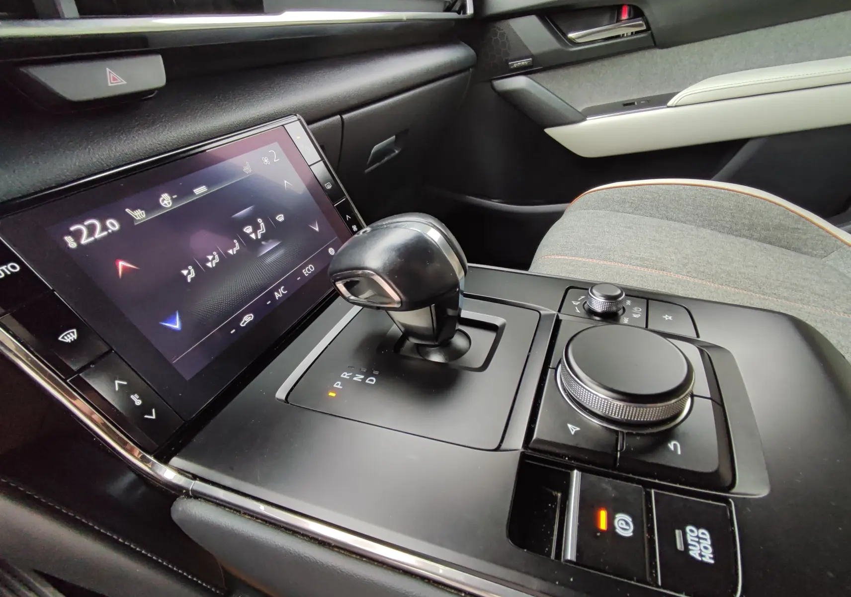 Vue rapprochée de la console centrale grise claire du Mazda MX-30 2023 avec levier de vitesse automatique et écran tactile.