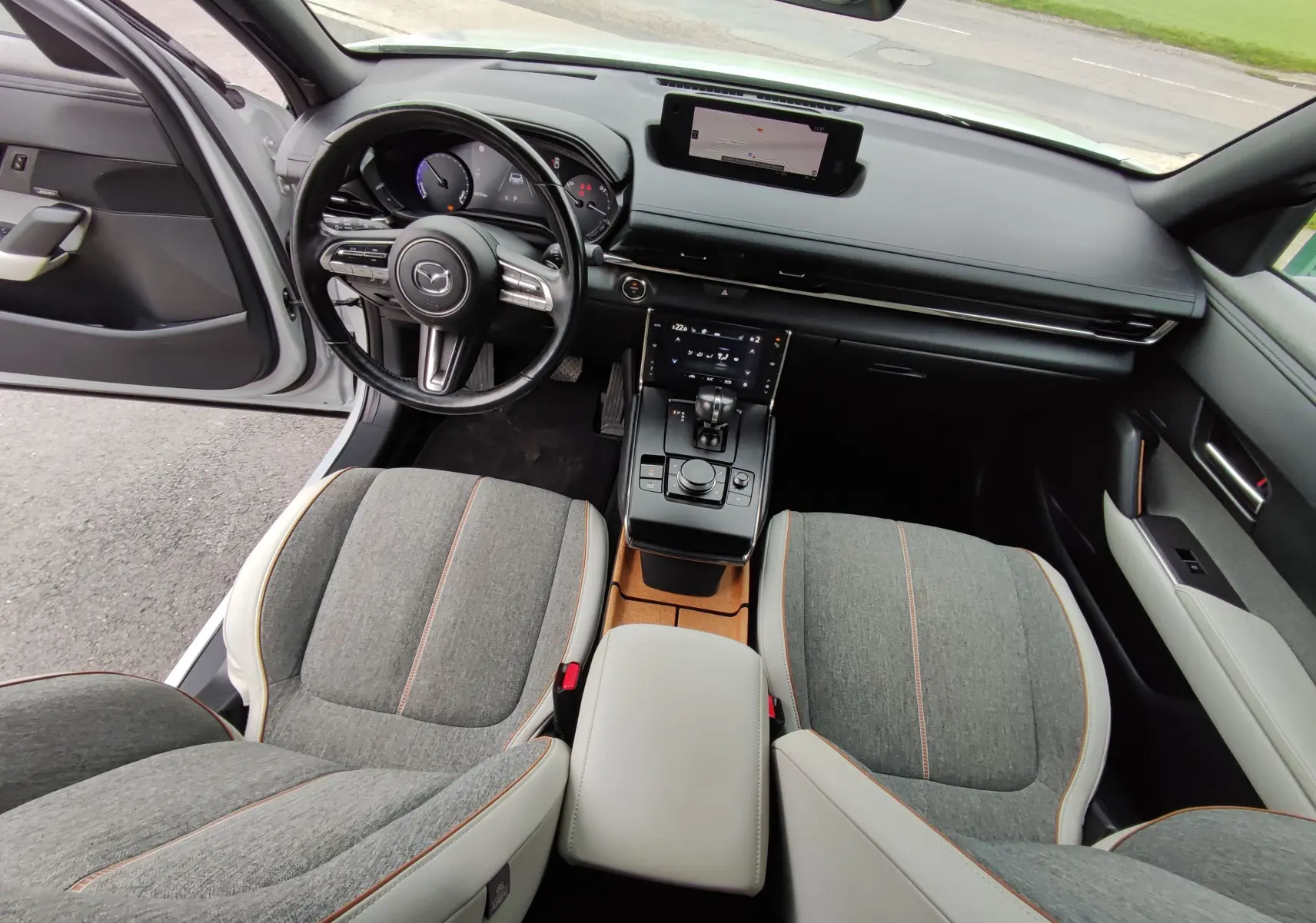 Vue intérieure avant du Mazda MX-30 gris clair 2023, avec sièges tissu gris, tableau de bord noir et écran tactile central.