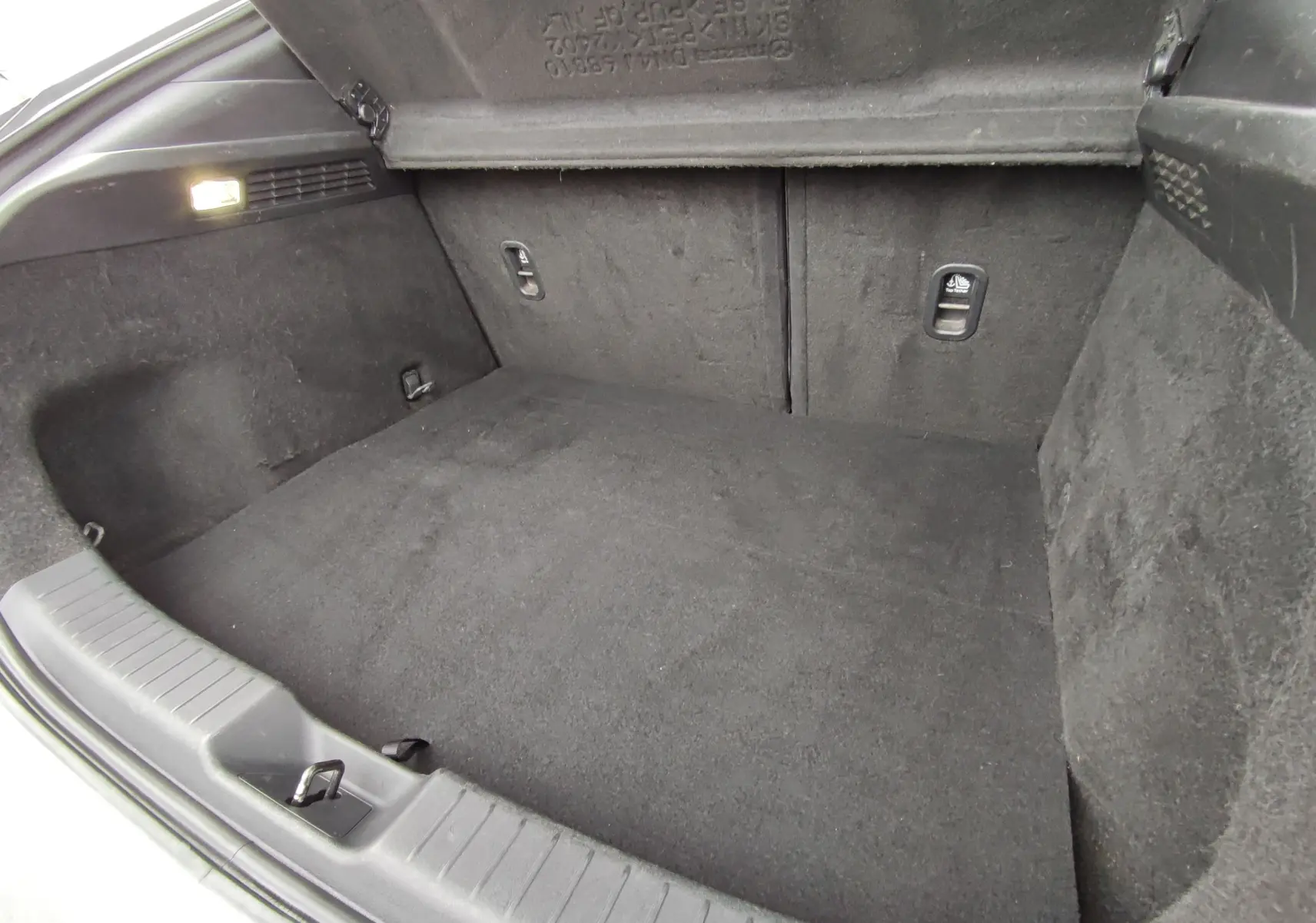 Coffre spacieux de Mazda MX-30 gris clair vu de l'intérieur, avec revêtement noir et éclairage latéral allumé.
