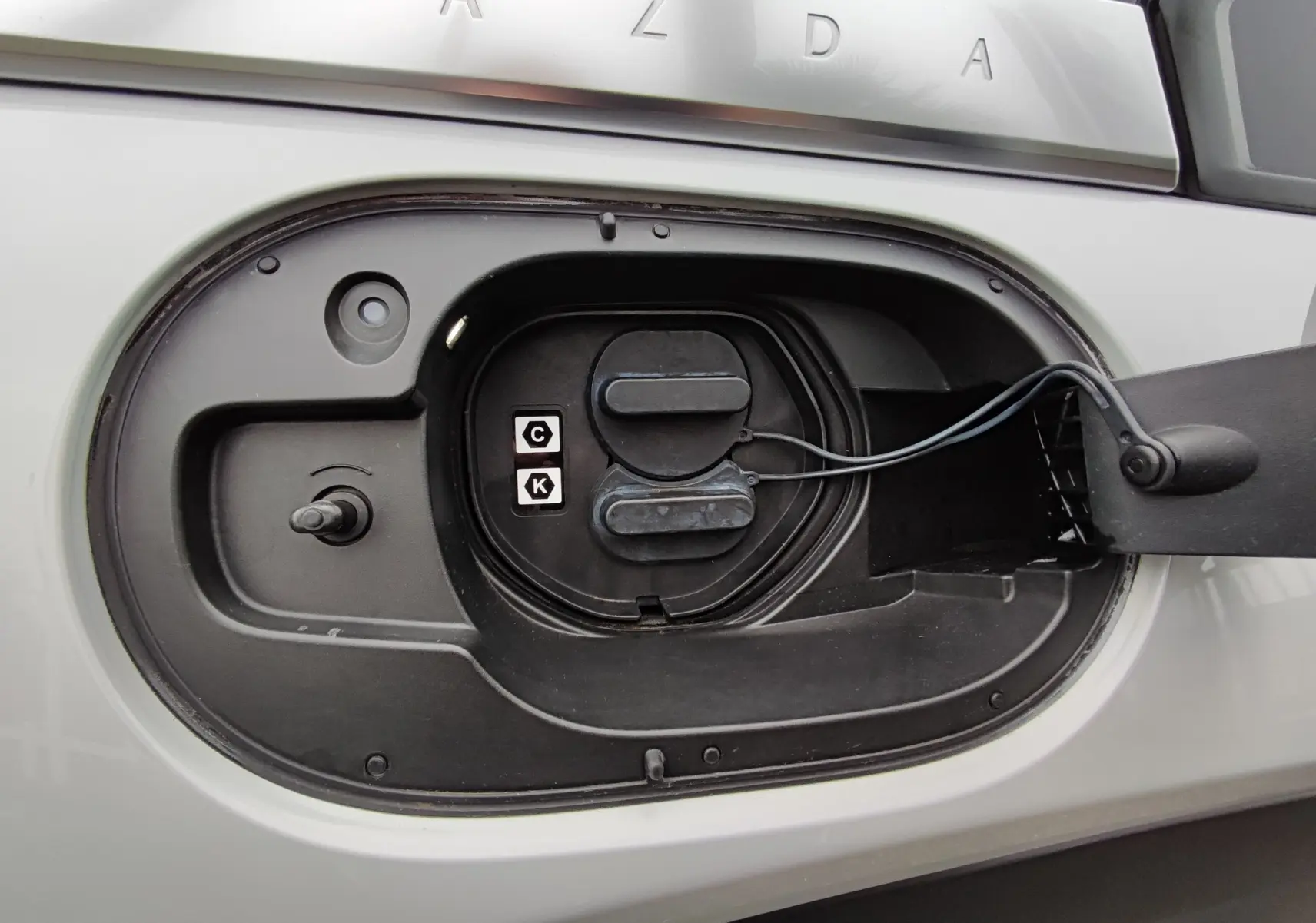 Gros plan sur la trappe de recharge électrique ouverte du Mazda MX-30 gris clair, montrant les connecteurs de charge.