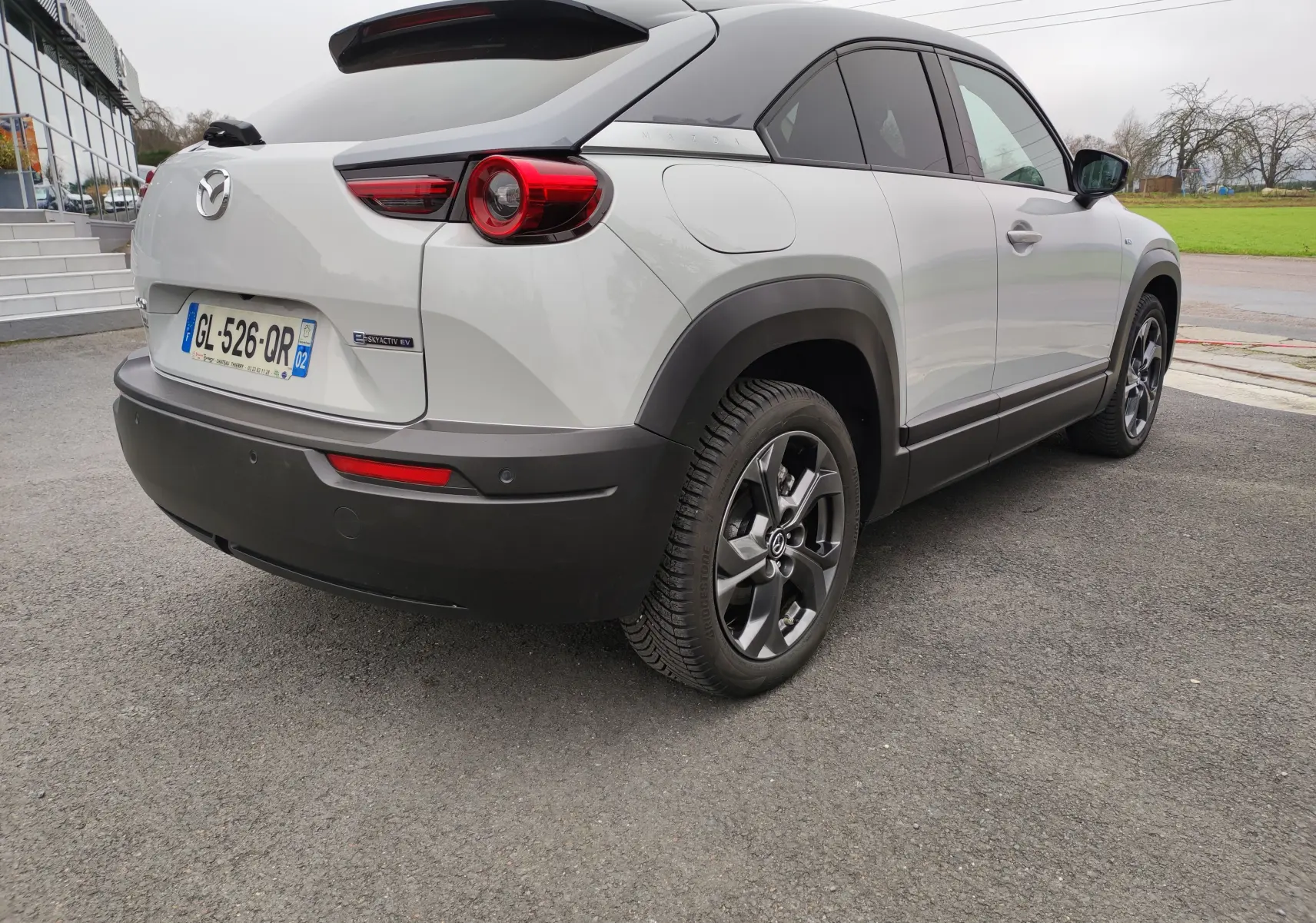 Vue 3/4 arrière droite d'une Mazda MX-30 gris clair électrique 2023 avec toit noir et jantes foncées.