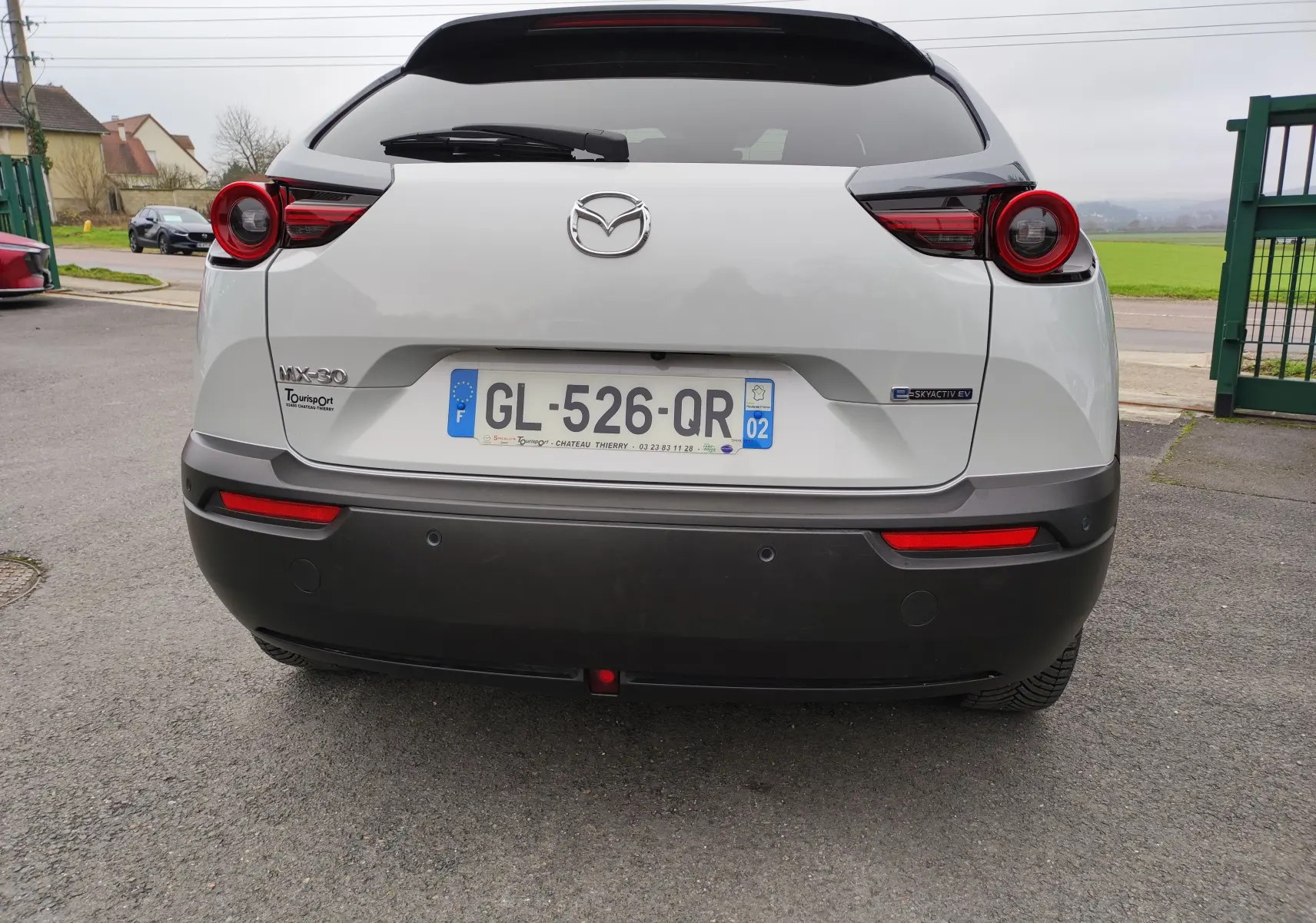Vue arrière d'une Mazda MX-30 gris clair 2023, avec feux arrière ronds et badge électrique E-SKYACTIV EV visible.