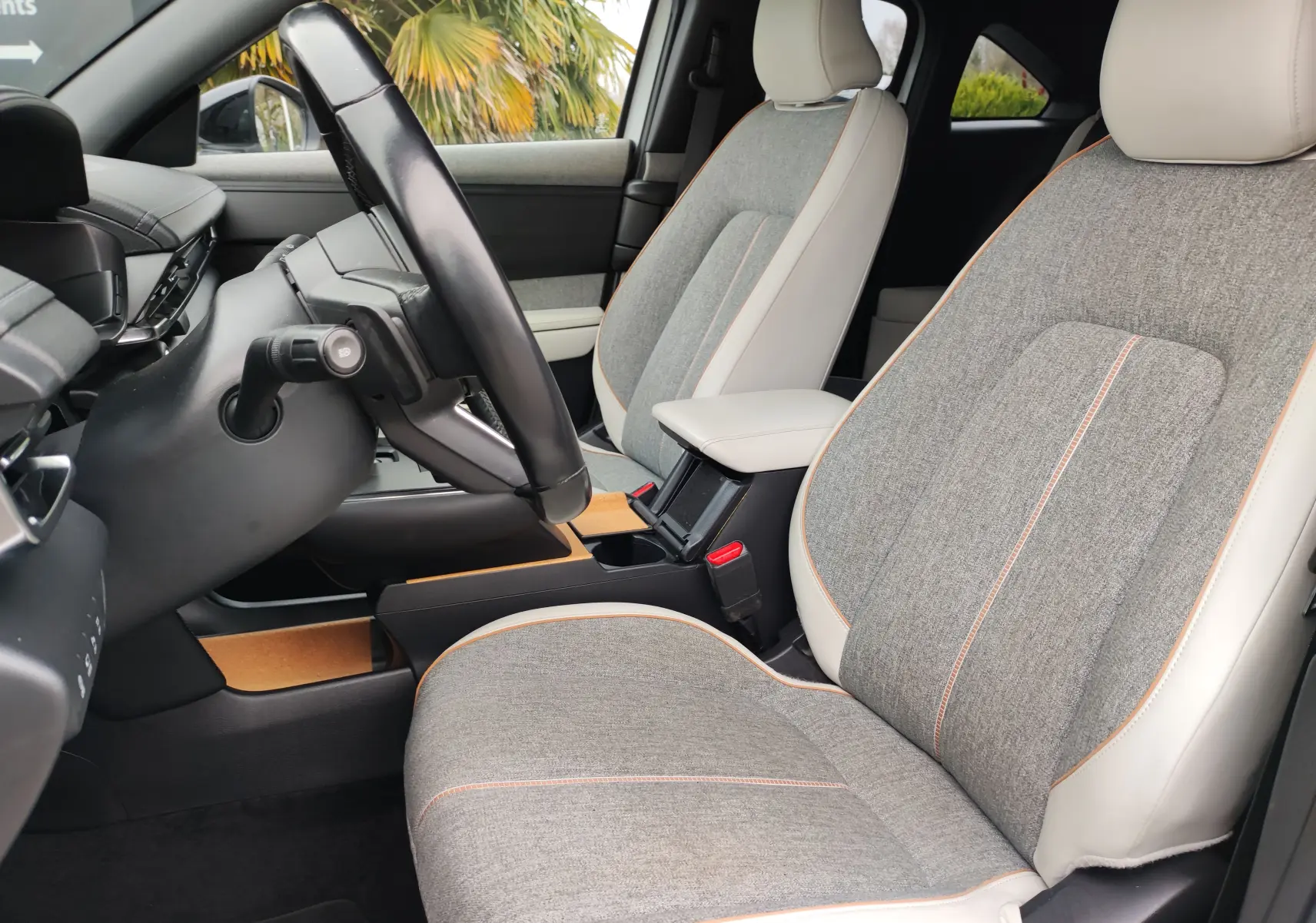 Vue intérieure côté conducteur du Mazda MX-30 gris clair 2023, sièges tissu gris avec surpiqûres orange et accoudoir central.