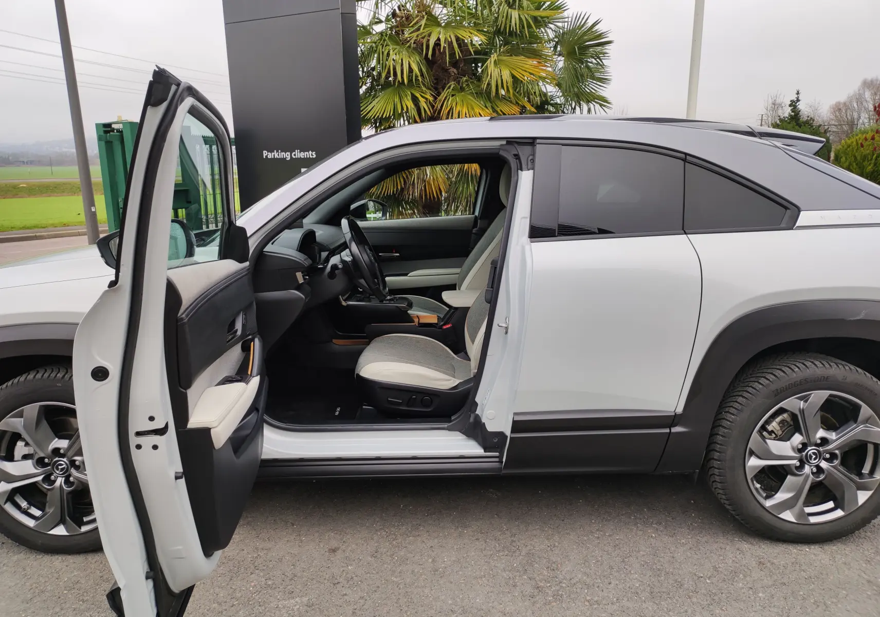 Vue latérale gauche du Mazda MX-30 gris clair 2023 avec porte avant ouverte dévoilant l’intérieur clair et moderne.