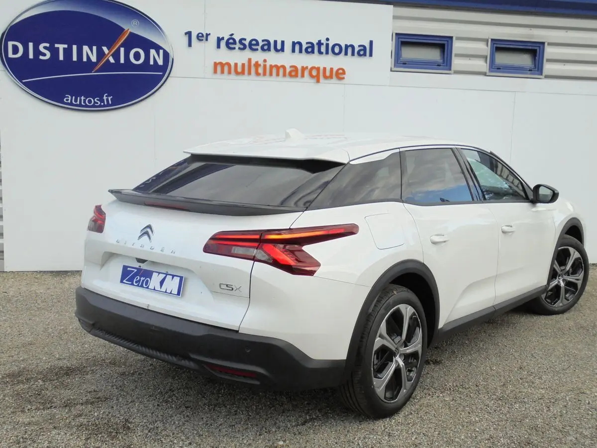 Vue 3/4 arrière droite d'une Citroën C5 X blanche nacrée avec feux arrière LED et jantes alliage noires.