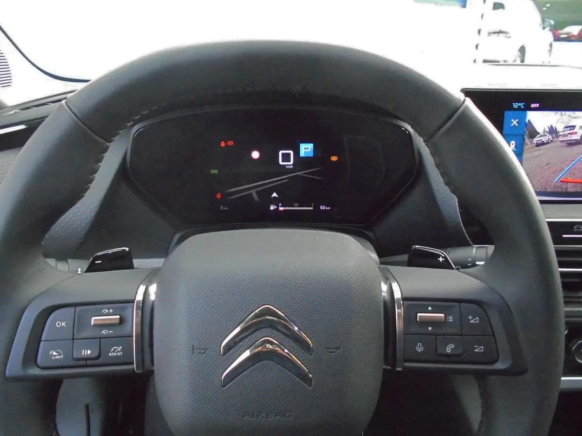 Vue rapprochée du volant noir de la Citroën C5 X avec commandes intégrées et tableau de bord numérique allumé.