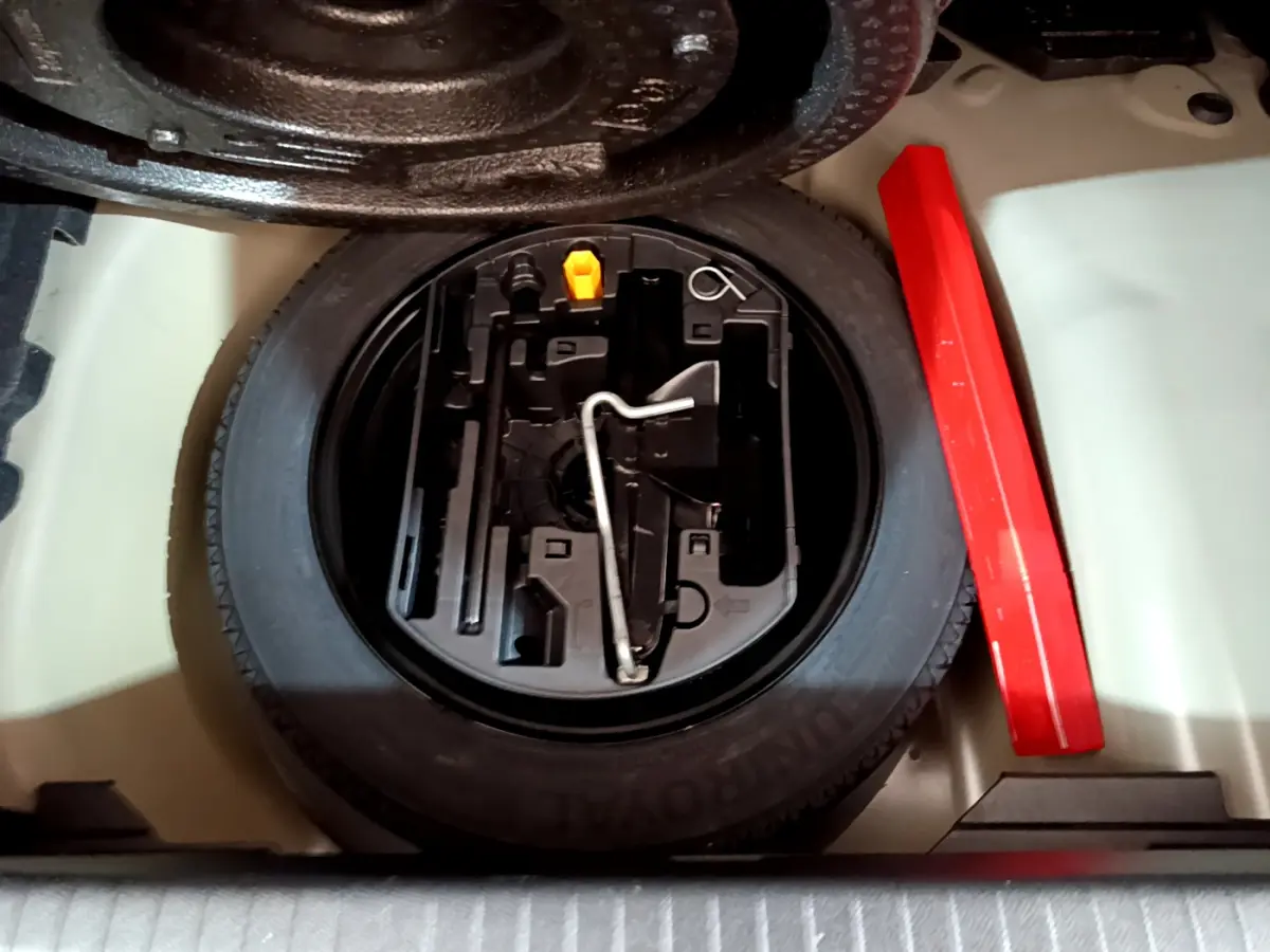 Vue rapprochée de la roue de secours et des outils de bord dans le coffre d'une Peugeot 208 gris foncé 2022.