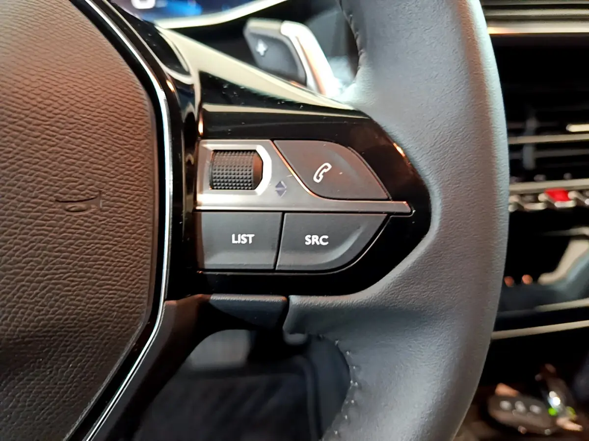 Gros plan sur les commandes gauche du volant cuir noir de la Peugeot 208 gris foncé, boutons LIST et SRC visibles.