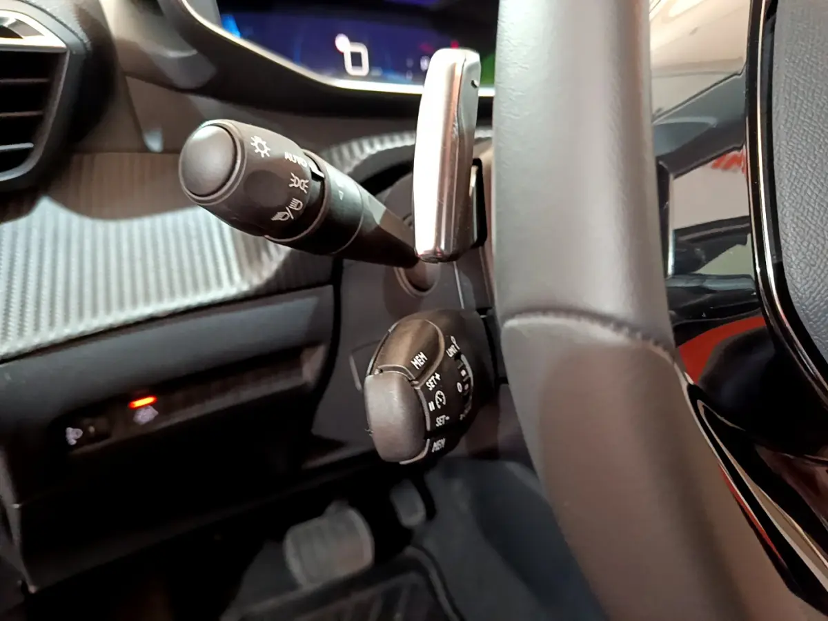 Gros plan intérieur sur la colonne de direction et commandes au volant cuir noir de la Peugeot 208 gris foncé.