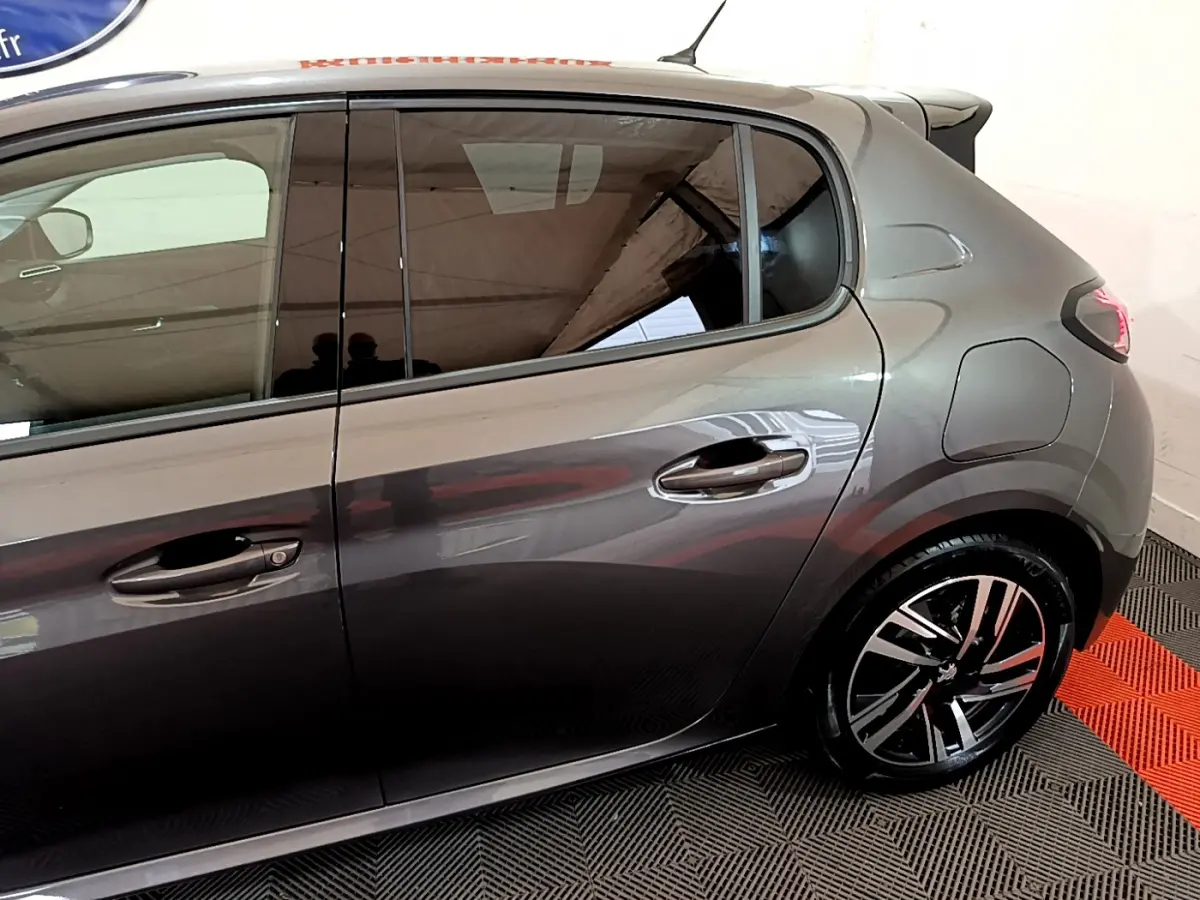 Vue latérale droite d'une Peugeot 208 gris foncé avec jantes alliage et poignées de porte chromées.