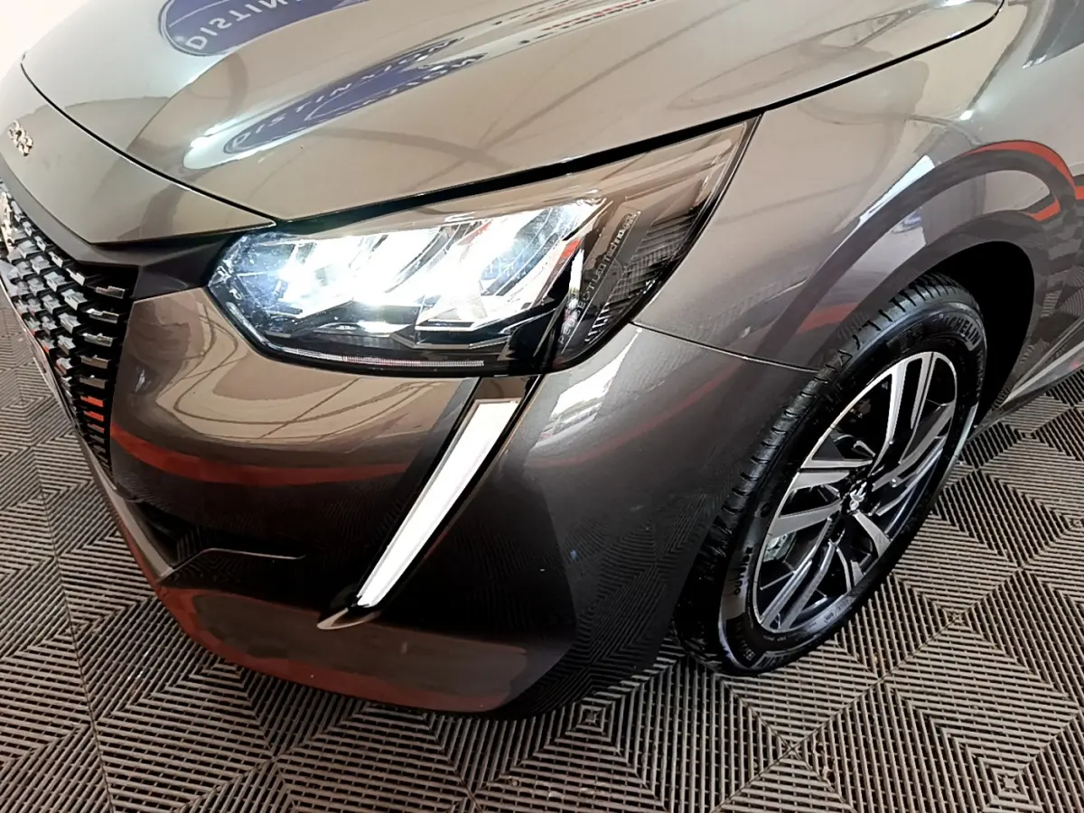 Vue 3/4 avant droit d'une Peugeot 208 gris foncé avec phares LED allumés et jante alliage visible.