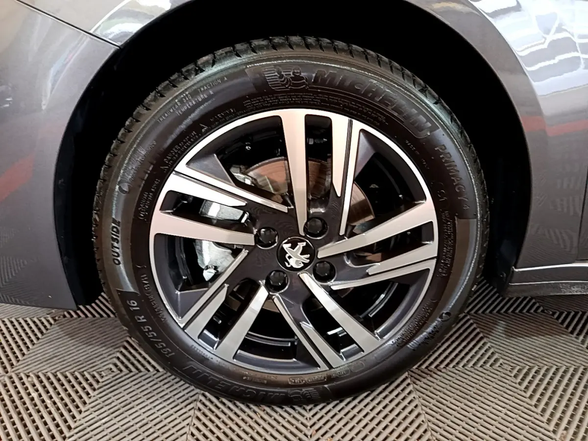 Gros plan sur la roue avant droite d’une Peugeot 208 gris foncé, avec jante alliage noire et argentée.