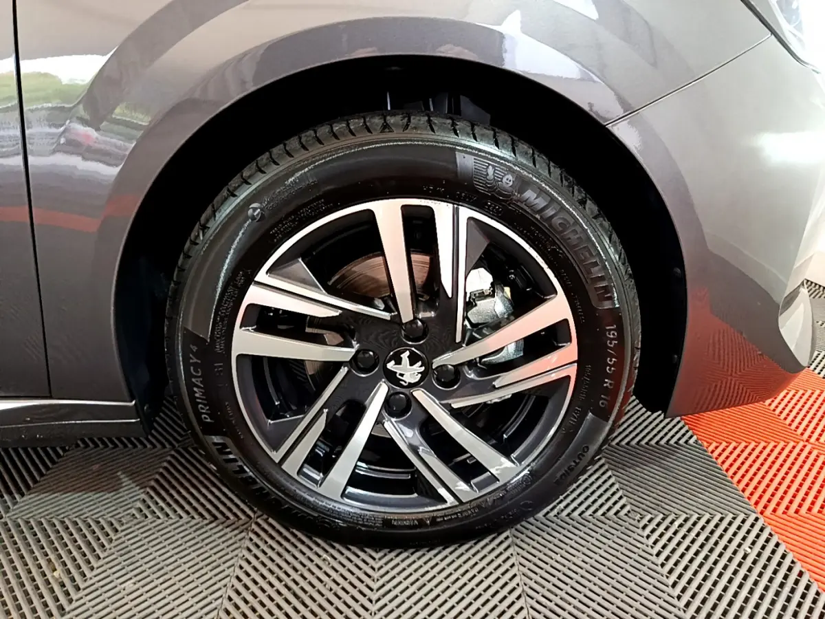 Gros plan sur la roue avant droite d’une Peugeot 208 gris foncé, jante alliage au design moderne à 5 branches doubles.