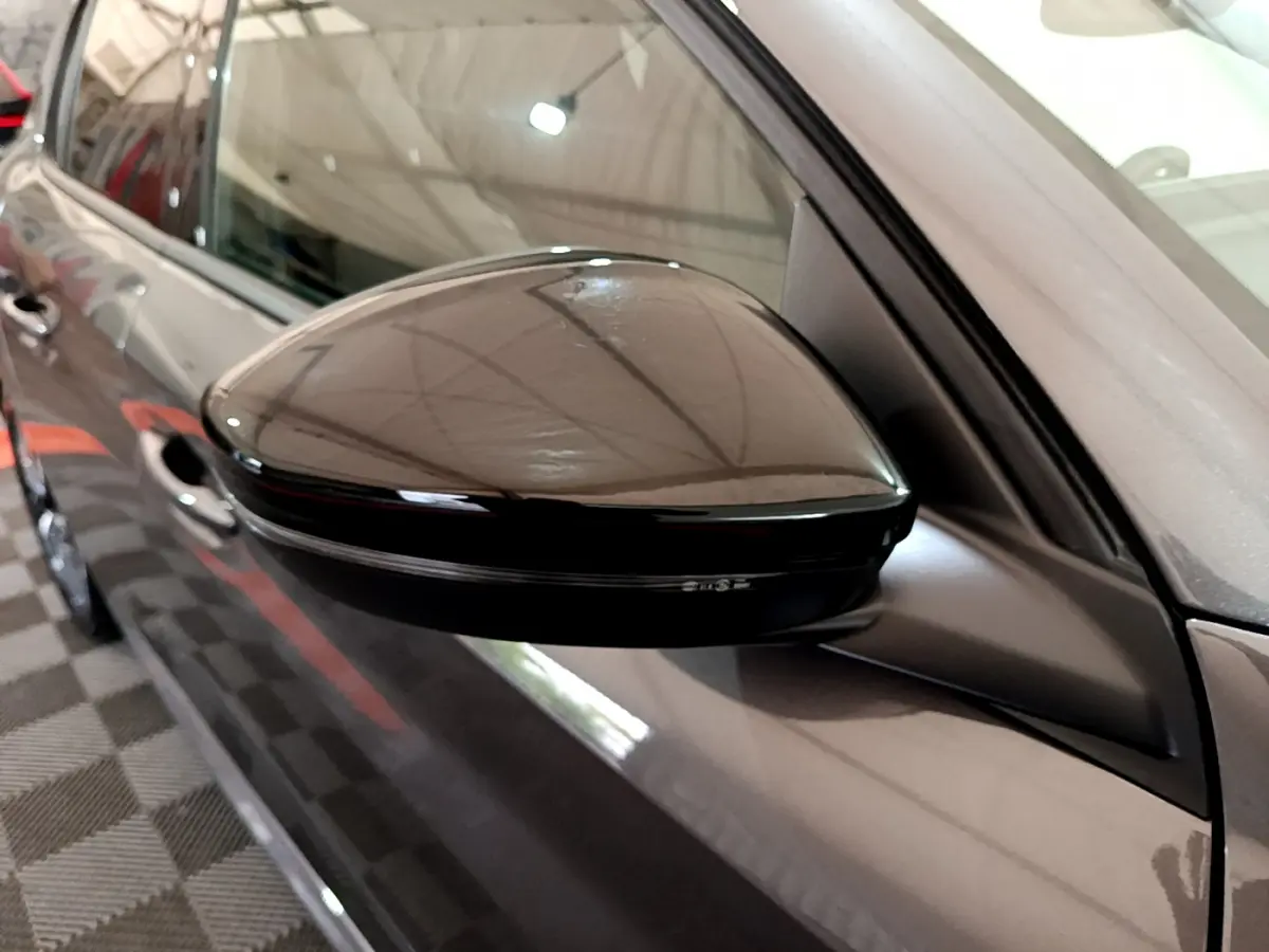 Gros plan sur le rétroviseur droit noir brillant d’une Peugeot 208 gris foncé vue de côté en intérieur.
