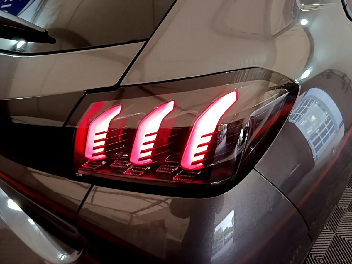 Gros plan sur le feu arrière droit rouge d’une Peugeot 208 gris foncé, soulignant ses lignes modernes et lumineuses.