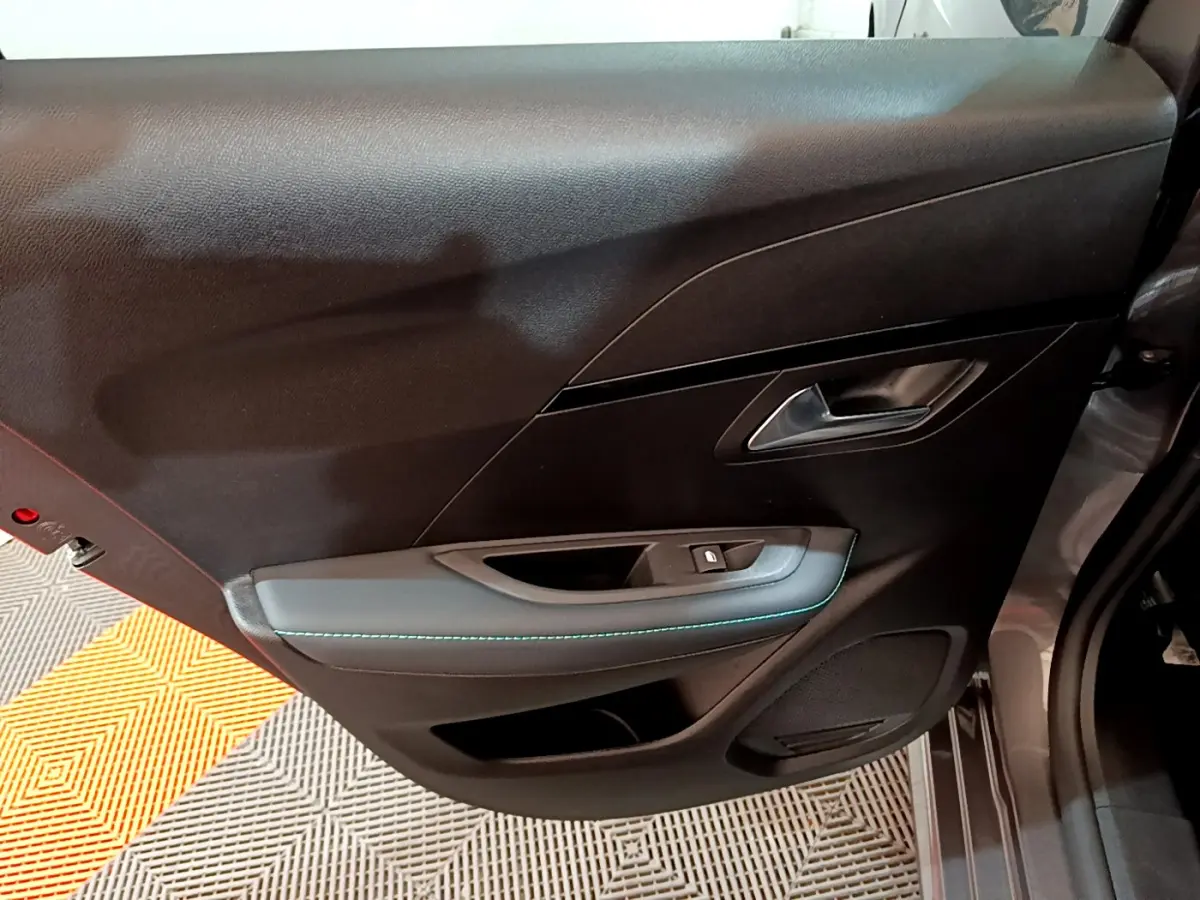 Gros plan sur la porte intérieure côté gauche de la Peugeot 208 gris foncé, avec surpiqûres bleues et poignée argentée.