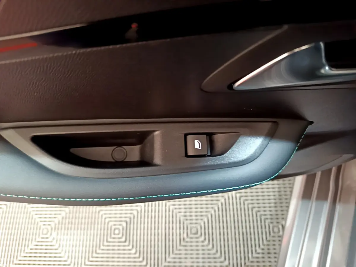 Gros plan sur la commande de verrouillage de porte côté conducteur d'une Peugeot 208 gris foncé avec surpiqûres bleues.