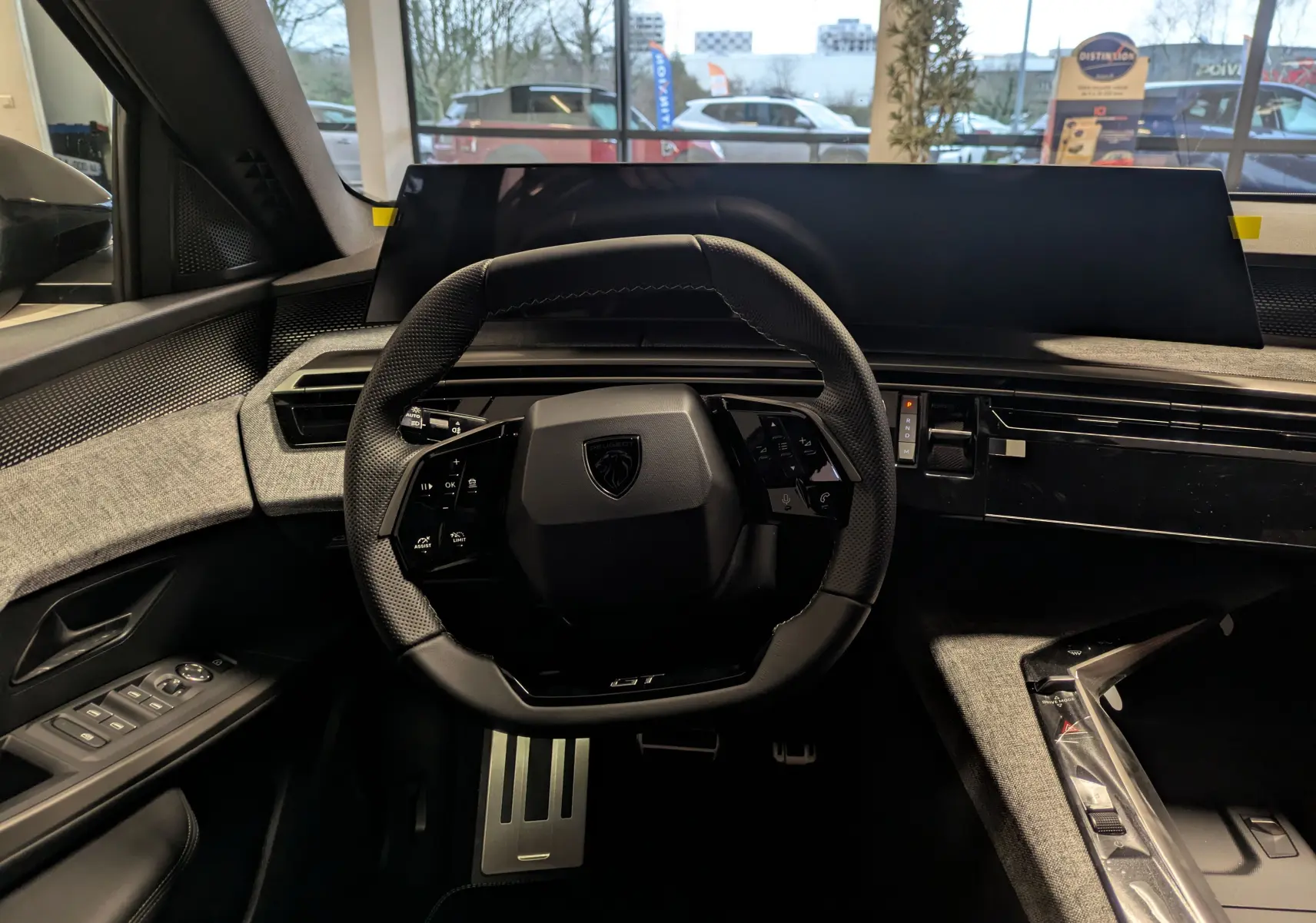 Vue intérieure centrée sur le volant GT et le tableau de bord numérique du Peugeot 3008 Hybrid gris titane, avec pédalier alu visible.