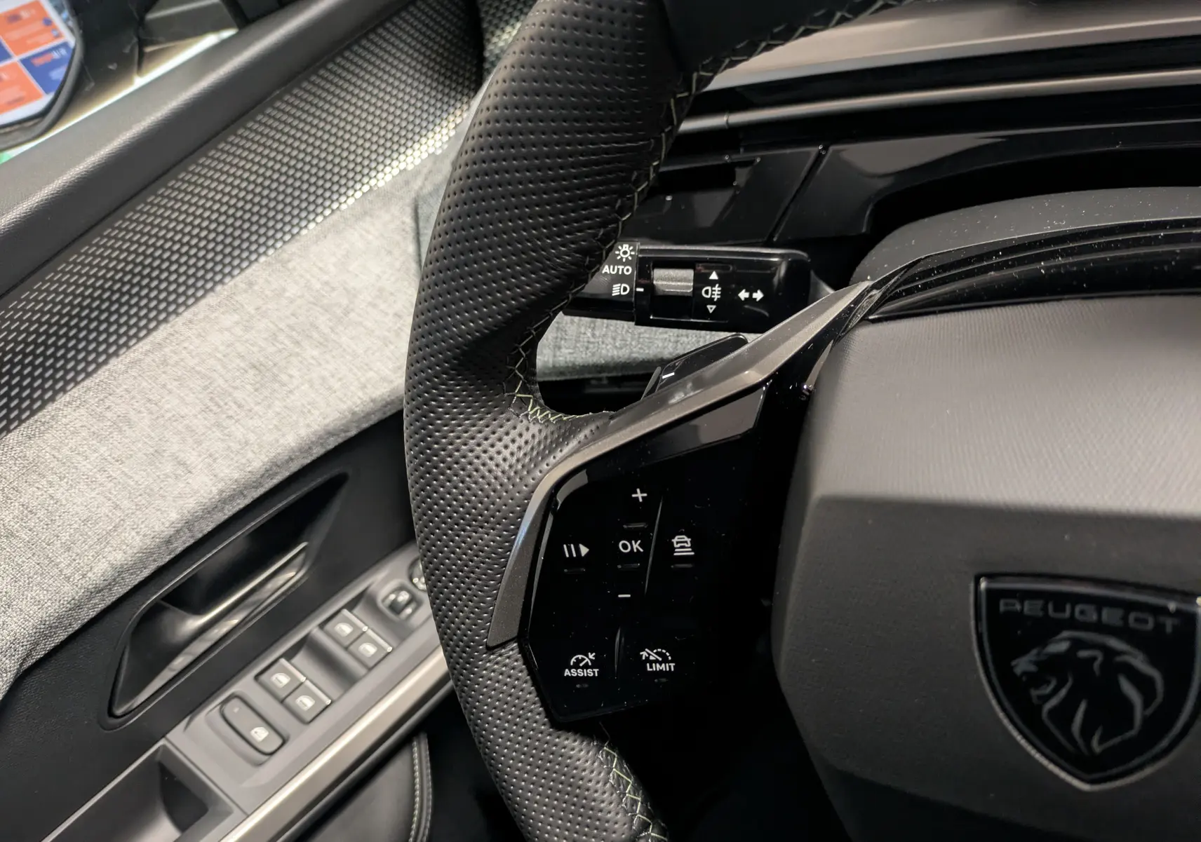 Gros plan sur le volant perforé noir avec surpiqûres vertes et commandes intégrées du Peugeot 3008 Hybrid 2025.