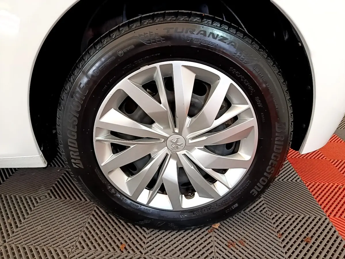 Gros plan sur la roue avant droite d'une Peugeot 208 blanche, avec jante alliage et pneu Bridgestone.
