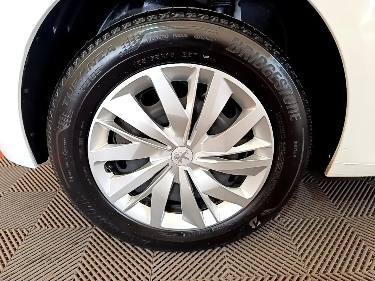 Gros plan sur la roue avant droite blanche d'une Peugeot 208 1.2 PT 75 S&S Premium avec jante argentée à design moderne.