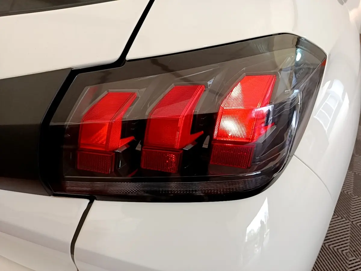 Gros plan sur le feu arrière droit rouge et noir d'une Peugeot 208 blanche, soulignant les lignes anguleuses du design.