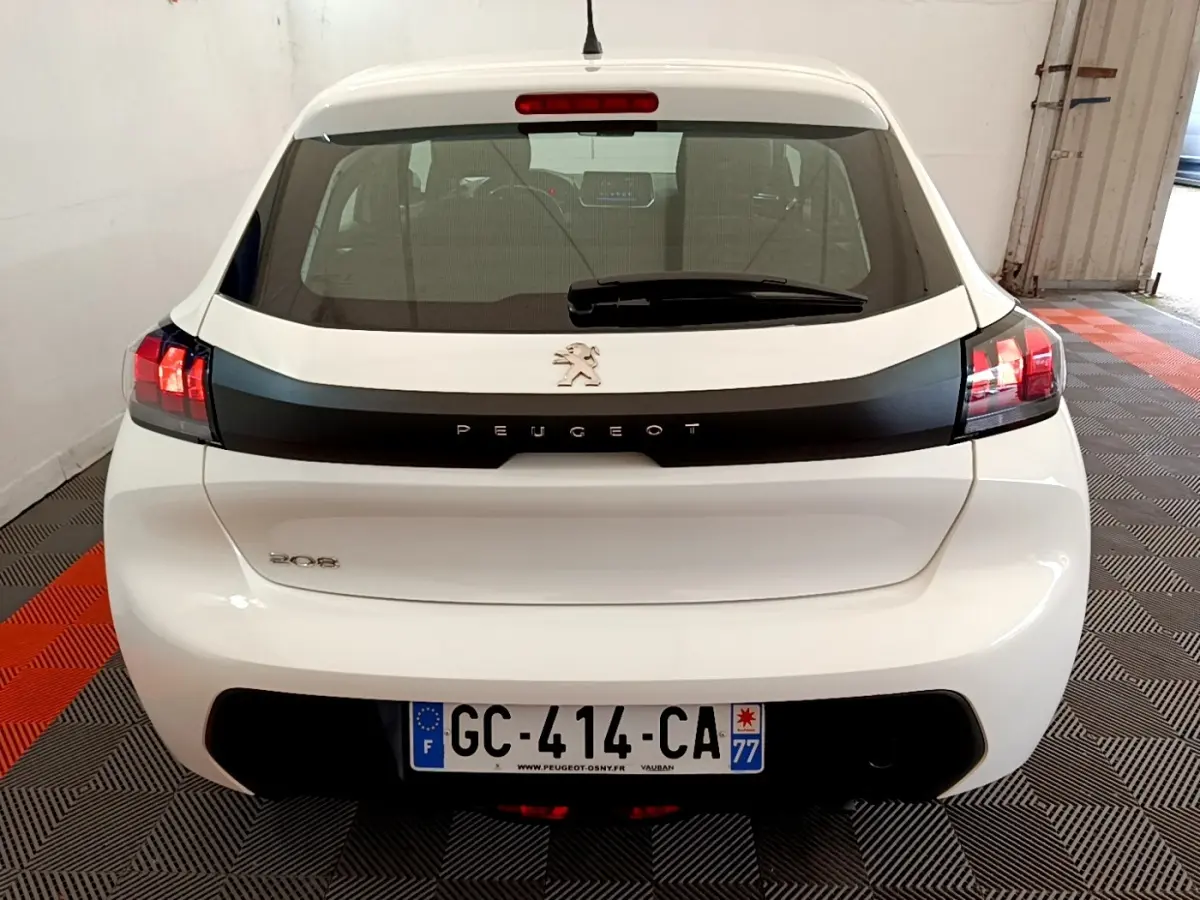 Vue arrière d'une Peugeot 208 blanche avec bande noire distinctive et feux arrière allumés en intérieur.